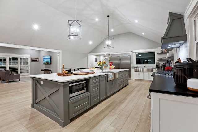 kitchen featuring premium range hood, built in appliances, light hardwood / wood-style flooring, gray cabinets, and an island with sink