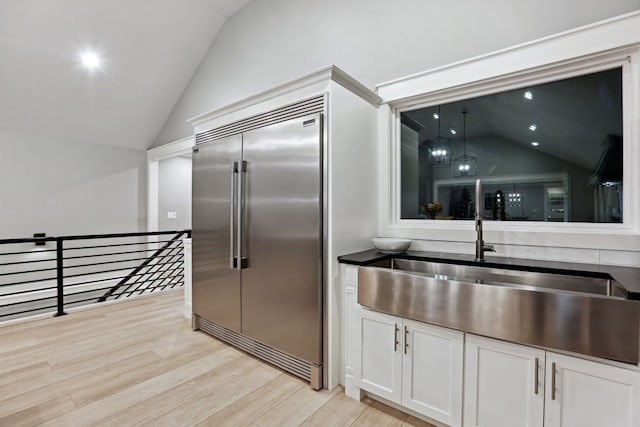 kitchen featuring light wood-type flooring, white cabinetry, vaulted ceiling, and built in fridge