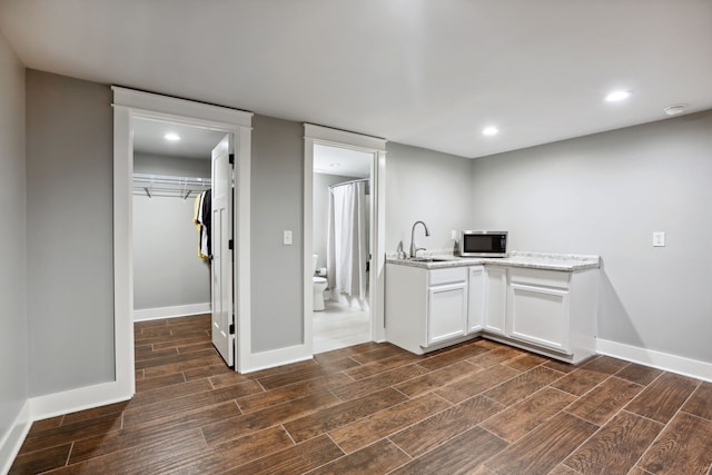 kitchen with light stone countertops, white cabinetry, dark wood-type flooring, and sink