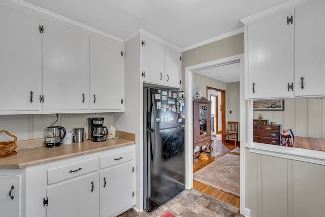 kitchen featuring white cabinetry, black fridge, light wood-type flooring, and ornamental molding