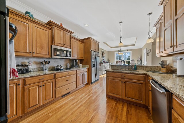 kitchen with sink, decorative light fixtures, a tray ceiling, appliances with stainless steel finishes, and light wood-type flooring