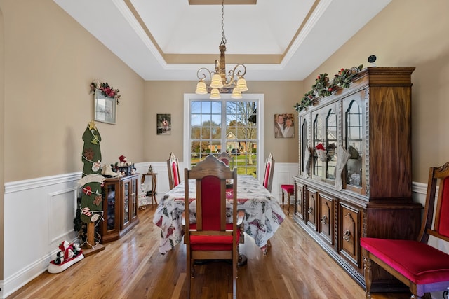 dining room with a raised ceiling, an inviting chandelier, light hardwood / wood-style flooring, and crown molding