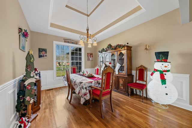 dining space featuring hardwood / wood-style floors, an inviting chandelier, and a raised ceiling