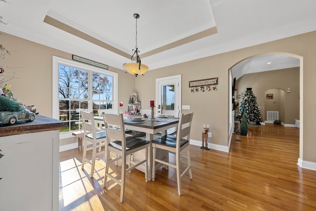 dining space featuring light wood-type flooring, a raised ceiling, and ornamental molding