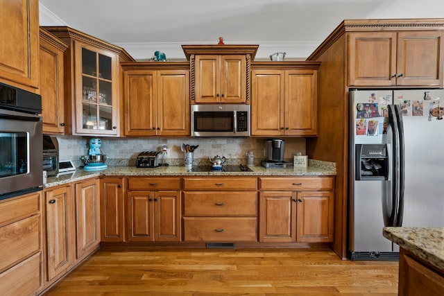 kitchen featuring tasteful backsplash, light stone counters, ornamental molding, stainless steel appliances, and light hardwood / wood-style flooring