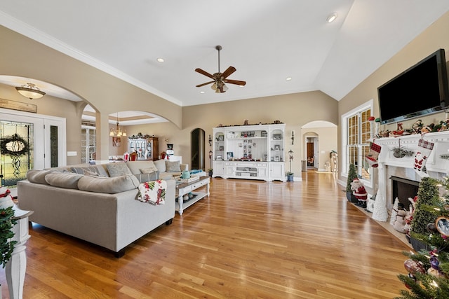 living room with ceiling fan with notable chandelier, light wood-type flooring, crown molding, and vaulted ceiling