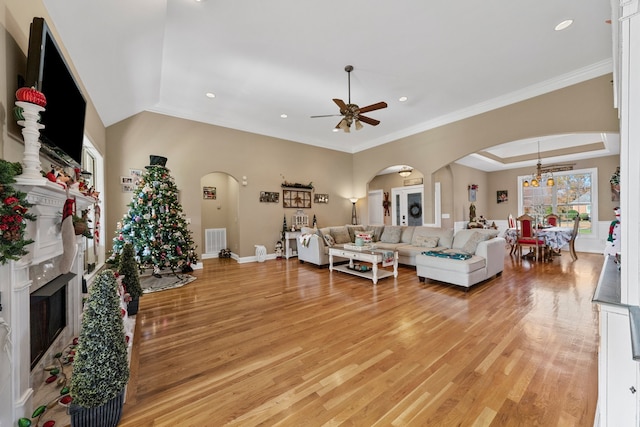 living room featuring ceiling fan with notable chandelier, light hardwood / wood-style floors, a raised ceiling, and ornamental molding