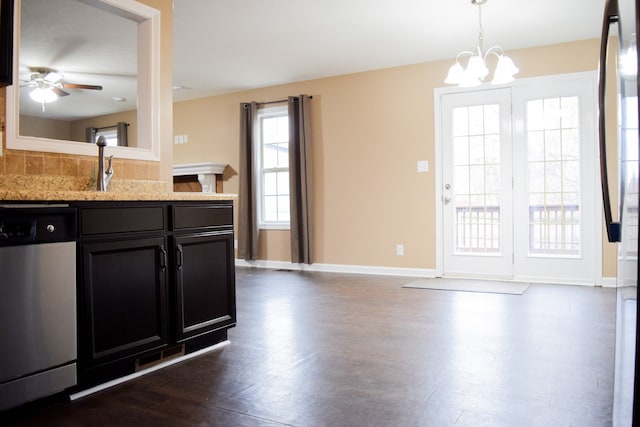 kitchen featuring pendant lighting, dark wood-type flooring, ceiling fan with notable chandelier, stainless steel dishwasher, and light stone counters