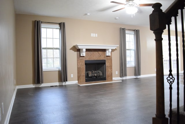 unfurnished living room with ceiling fan, plenty of natural light, dark wood-type flooring, and a tiled fireplace