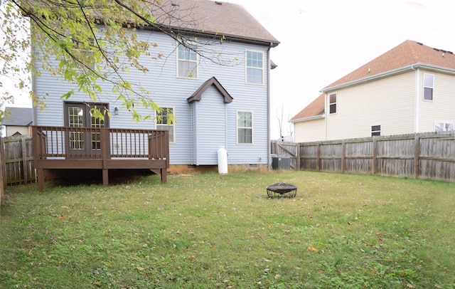 rear view of property featuring a lawn, a deck, an outdoor fire pit, and central air condition unit