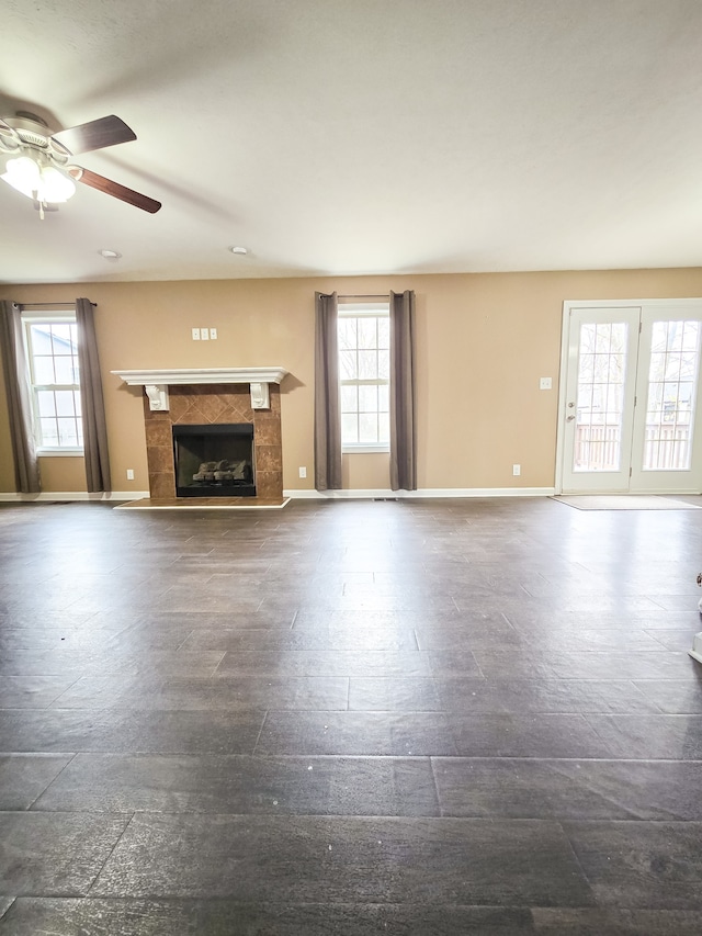 unfurnished living room featuring a tiled fireplace, a wealth of natural light, and ceiling fan