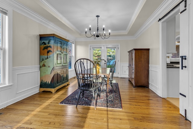 dining room with a barn door, crown molding, light hardwood / wood-style flooring, and an inviting chandelier