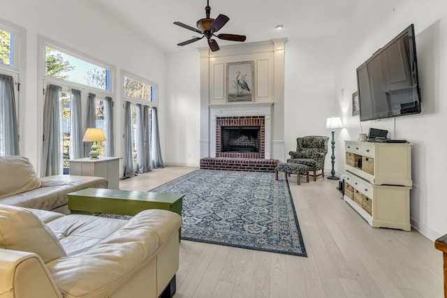 living room with ceiling fan, light hardwood / wood-style flooring, a high ceiling, and a brick fireplace