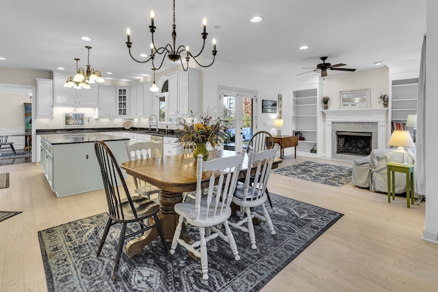 dining room with built in shelves, light hardwood / wood-style floors, sink, and ceiling fan with notable chandelier