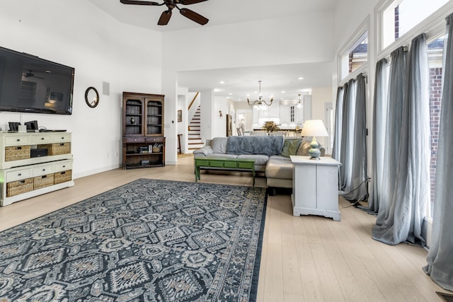 living room featuring ceiling fan with notable chandelier, a high ceiling, and light hardwood / wood-style flooring