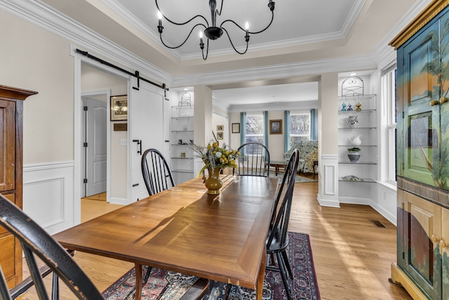 dining area featuring built in shelves, a barn door, a notable chandelier, light hardwood / wood-style floors, and ornamental molding