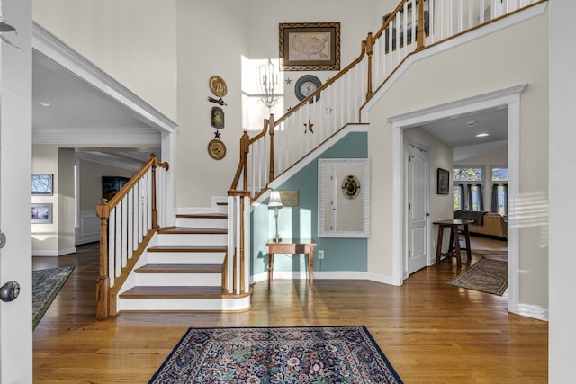 entrance foyer with a towering ceiling, ornamental molding, and hardwood / wood-style flooring