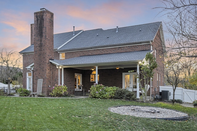 back house at dusk with ceiling fan, a yard, and central AC