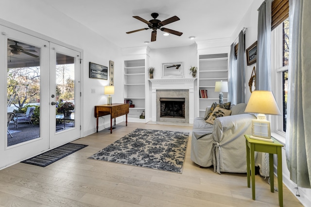 living room featuring ceiling fan, built in features, light wood-type flooring, and a wealth of natural light