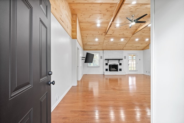 unfurnished living room featuring ceiling fan, a brick fireplace, vaulted ceiling with beams, wood ceiling, and light wood-type flooring