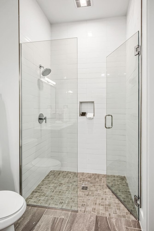 bathroom with hardwood / wood-style flooring, a shower with door, and toilet