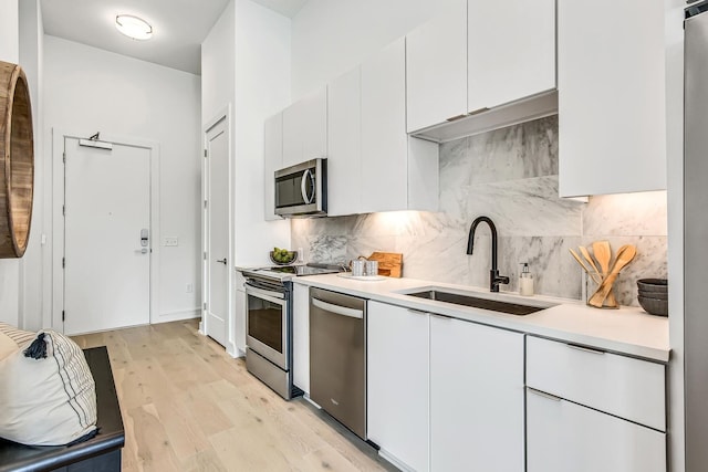 kitchen with white cabinetry, sink, stainless steel appliances, and light hardwood / wood-style floors