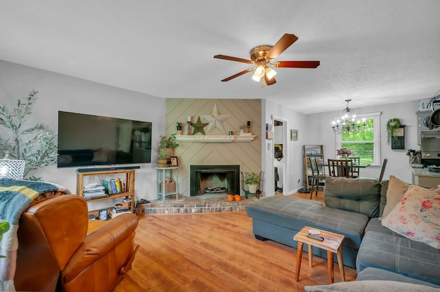 living room with hardwood / wood-style floors, ceiling fan with notable chandelier, wooden walls, a brick fireplace, and a textured ceiling