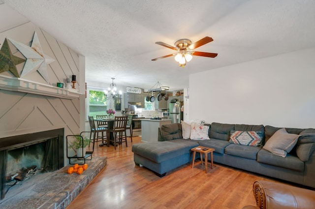 living room featuring ceiling fan with notable chandelier, a fireplace, wood-type flooring, and a textured ceiling