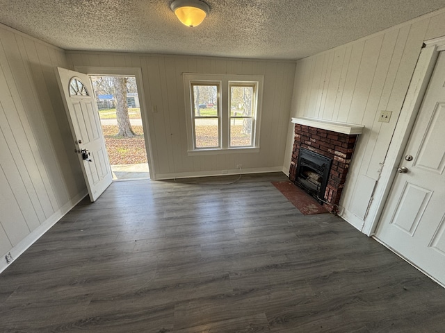 unfurnished living room featuring wood walls, dark hardwood / wood-style flooring, a textured ceiling, and a brick fireplace