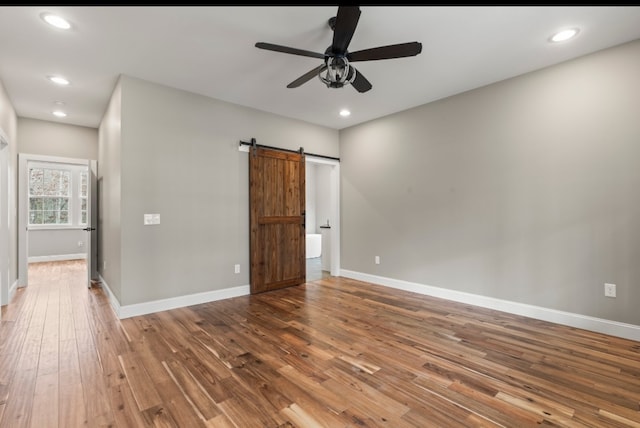 spare room featuring ceiling fan, a barn door, and wood-type flooring