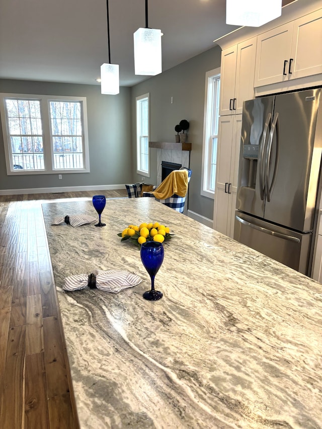 kitchen featuring light stone countertops, stainless steel fridge, a fireplace, dark hardwood / wood-style floors, and white cabinetry