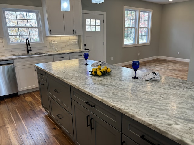 kitchen featuring stainless steel dishwasher, plenty of natural light, light stone counters, and sink