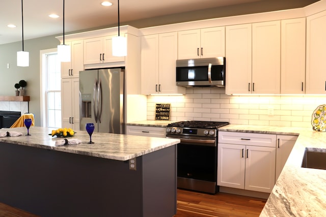 kitchen with light stone countertops, hanging light fixtures, dark hardwood / wood-style flooring, white cabinets, and appliances with stainless steel finishes