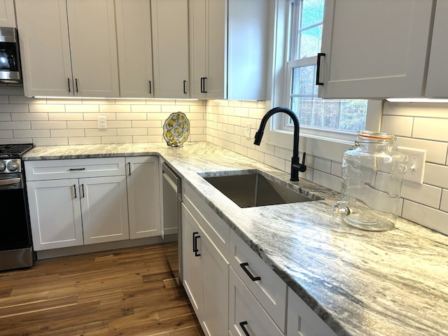 kitchen with light stone countertops, appliances with stainless steel finishes, dark wood-type flooring, sink, and white cabinetry