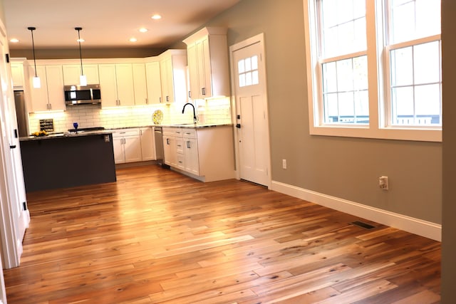 kitchen featuring a wealth of natural light, white cabinets, stainless steel appliances, and decorative light fixtures