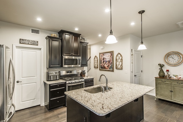 kitchen featuring light stone countertops, sink, stainless steel appliances, pendant lighting, and a kitchen island with sink