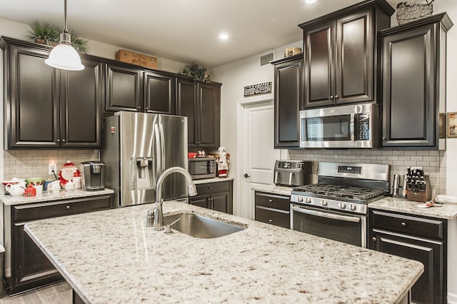 kitchen with backsplash, sink, light stone countertops, decorative light fixtures, and stainless steel appliances