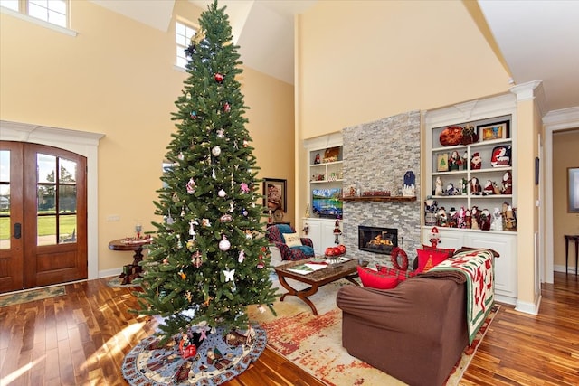 living room with hardwood / wood-style flooring, a stone fireplace, and a towering ceiling