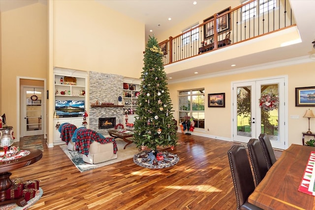 living room with french doors, crown molding, hardwood / wood-style floors, a towering ceiling, and a fireplace