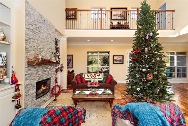 living room with wood-type flooring, a towering ceiling, a stone fireplace, and crown molding