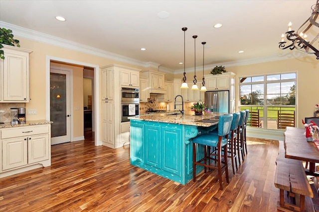 kitchen with light stone countertops, hanging light fixtures, dark hardwood / wood-style flooring, a kitchen island with sink, and appliances with stainless steel finishes