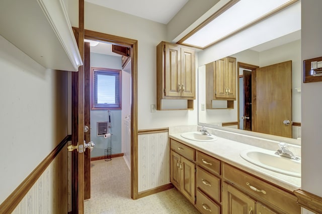 full bathroom featuring double vanity, wainscoting, a sink, and wallpapered walls