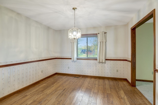 spare room featuring an inviting chandelier and light wood-type flooring