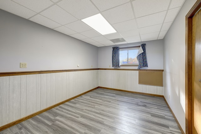 unfurnished room featuring a paneled ceiling, light hardwood / wood-style flooring, and wood walls