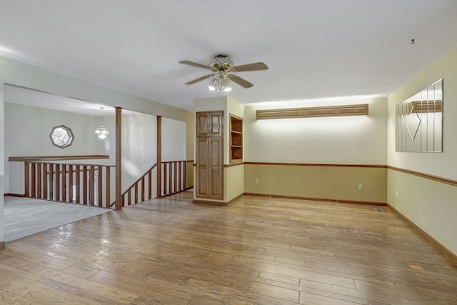 unfurnished room with ceiling fan with notable chandelier, light wood finished floors, and baseboards