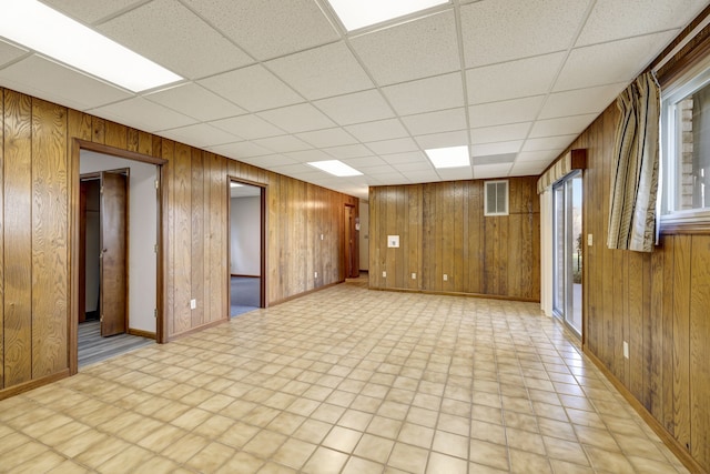 unfurnished room with baseboards, wooden walls, visible vents, and a drop ceiling