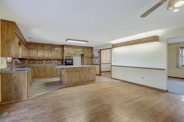 kitchen with a sink, baseboards, black oven, light wood finished floors, and tasteful backsplash