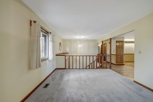 carpeted empty room with an inviting chandelier, visible vents, and baseboards