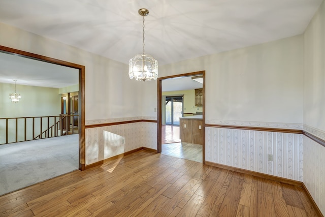 spare room with wallpapered walls, baseboards, wainscoting, hardwood / wood-style floors, and a chandelier