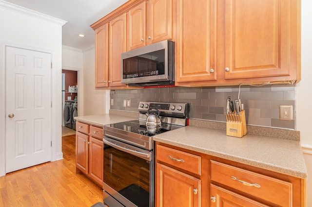 kitchen with tasteful backsplash, washing machine and dryer, crown molding, appliances with stainless steel finishes, and light wood-type flooring